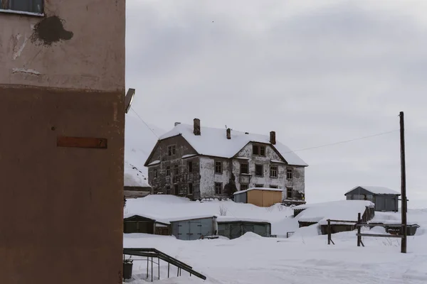 Old dilapidated and partially destroyed houses in which people still live in the village in the far north in winter under the thick slime of white snow