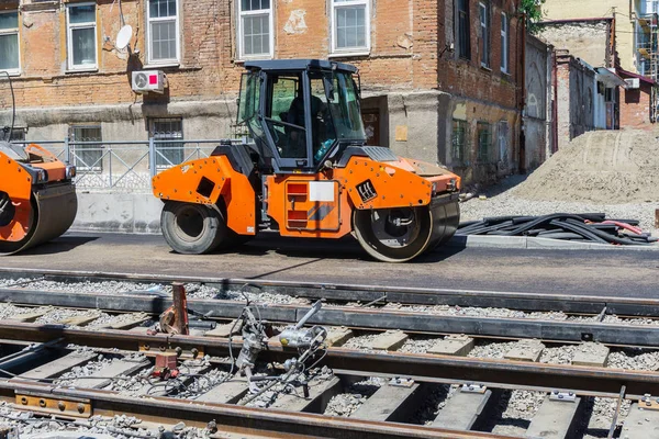 An orange construction roller compacts a new asphalt on a block in the center of the city near the new tram tracks