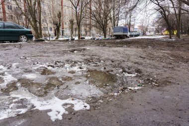 Islak bahçede kirli su birikintileri ve temizlenmemiş enkaz yere park etmiş arabaların yüksek katlı binalarla şehirde birinin yakınında kar kalıntıları yaylı