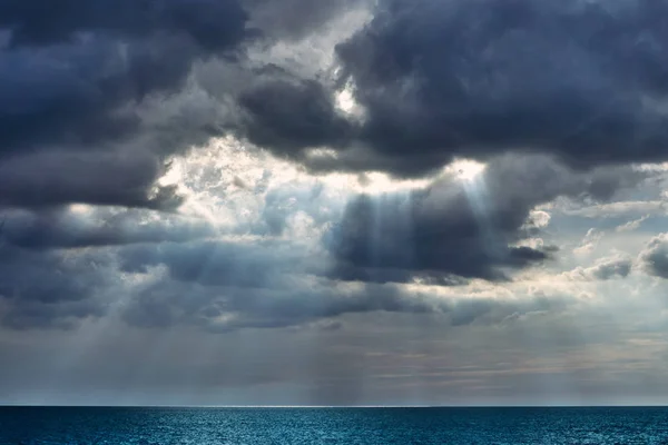 Large dark clouds over a calm blue sea cover the sun on a warm summer day