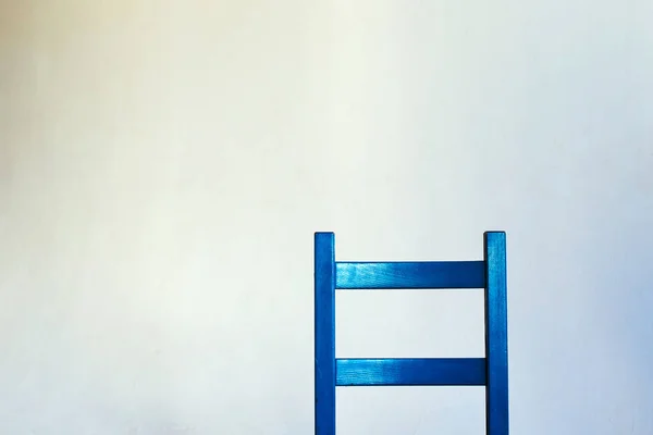 The back of the blue chair made of wood is located inside the room against a white lighted wall