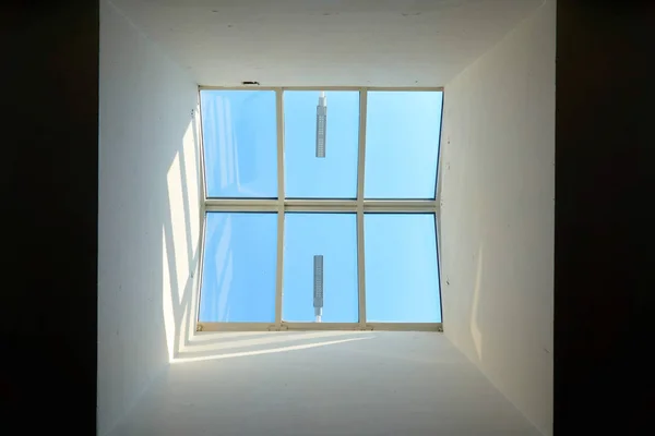 square window from where you can see a clear blue sky looking up in a modern designer\'s ceiling