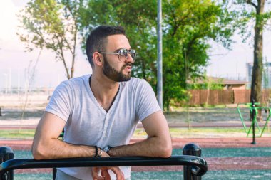 Genç bir adam fiziksel görünüm olarak iyi bir sakallı ve şehir parkı sıcak güneşli bir yaz aylarında sokakta simülatörleri trenlerde güneş gözlüğü