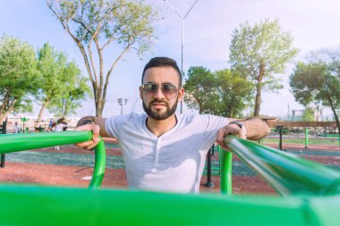 Genç bir adam fiziksel görünüm olarak iyi bir sakallı ve şehir parkı sıcak güneşli bir yaz aylarında sokakta simülatörleri trenlerde güneş gözlüğü