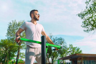 Genç bir adam fiziksel görünüm olarak iyi bir sakallı ve şehir parkı sıcak güneşli bir yaz aylarında sokakta simülatörleri trenlerde güneş gözlüğü