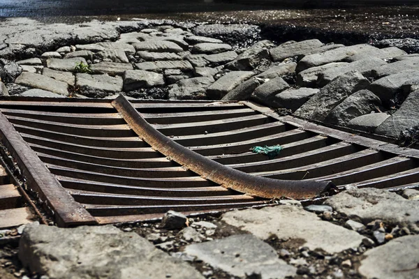 drainage sewer grate on the old road from the broken asphalt and paving blocks wet after the rain in one of the central streets of the city\'s greater