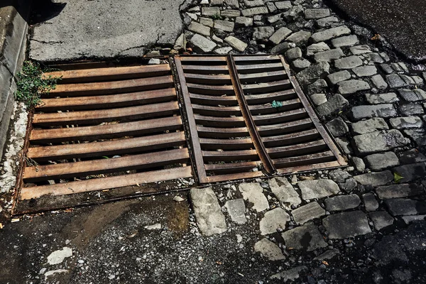 drainage sewer grate on the old road from the broken asphalt and paving blocks wet after the rain in one of the central streets of the city\'s greater