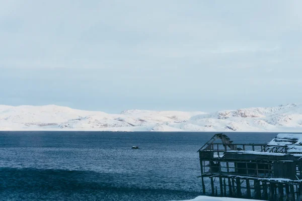 雪の降る冬の北部の村で海に漁船の古い木製の桟橋 — ストック写真