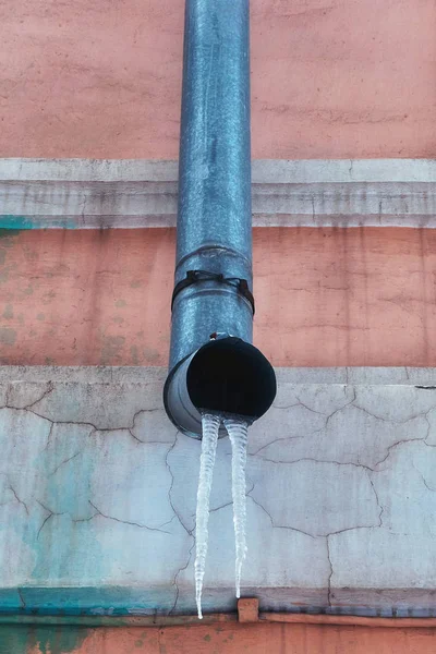 Icicle frozen in a drain and hanging on the edge of the pipe