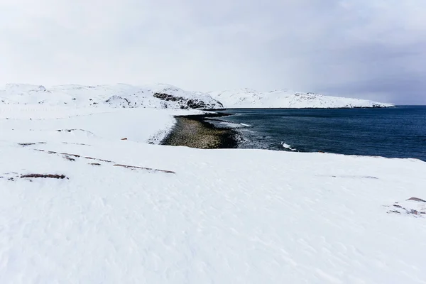 凍るような冬の白い雪の層の下の石と北極海の青の冷たい水と海岸 — ストック写真