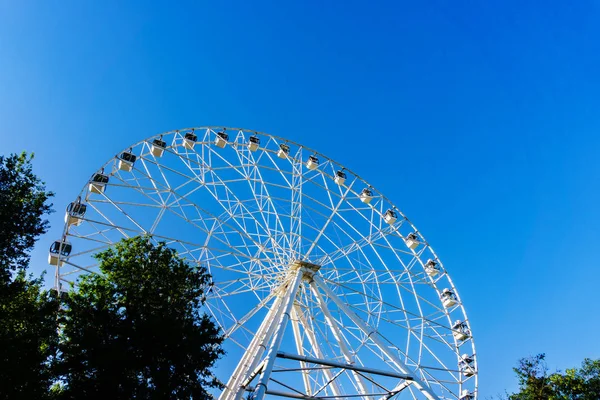 Egy új nagyon magas fehér Ferris kerék kényelmes fülkékkel az emberek lassan forog a kör közepén egy nagy város ellen, tiszta kék ég — Stock Fotó