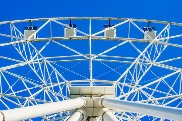 En ny mycket lång vit pariserhjul med bekväma bås för människor roterar långsamt i en cirkel i mitten av en storstad mot en klarblå himmel — Stockfoto