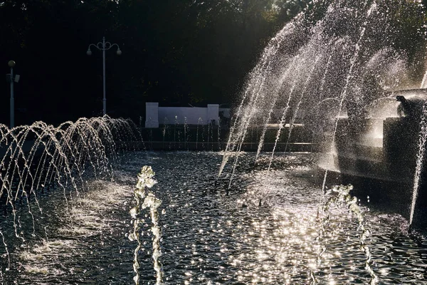 Vattenstrålar av en stor fontän glans i strålar i den centrala staden parkerar av staden i luften på en solig sommardag — Stockfoto