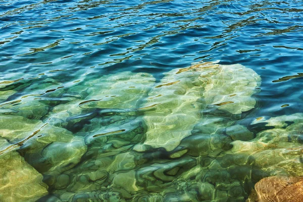 Kristallklara blå kallt vatten på en vild sjön i ett stenbrott utan personer med branta klippstränder och stora stenblock på en varm sommardag — Stockfoto