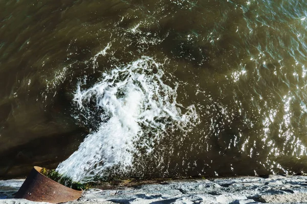 Discharge of sewage from a city pipe into a river on the embankment. Water blurred in long exposure photo. — Stock Photo, Image