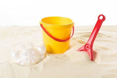 Kova ve kum üzerinde beyaz izole plastik oyuncaklar