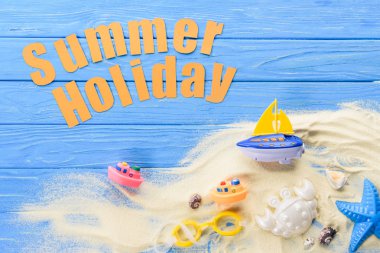 Beach toys by Summer holiday inscription on blue wooden background clipart