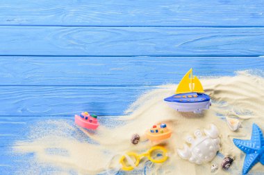 Beach toys in sand on blue wooden background clipart