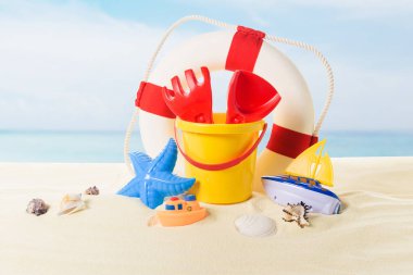 Life ring and beach toys in sand on blue sky background clipart