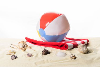 Beach ball on towel by seashells in sand isolated on white clipart