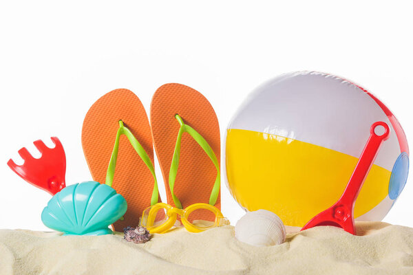 Beach ball and flip flops in sand isolated on white