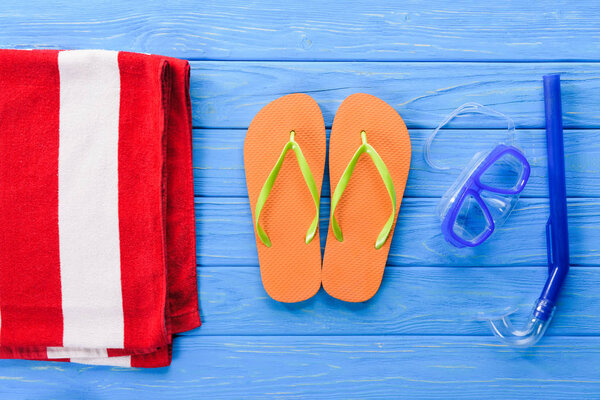 Flip flops with mask and towel on blue wooden background
