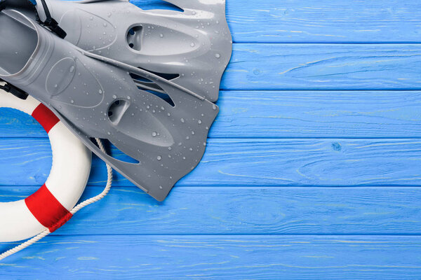 Swimming flippers and life ring on blue wooden background