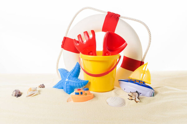 Life ring and beach toys in sand isolated on white