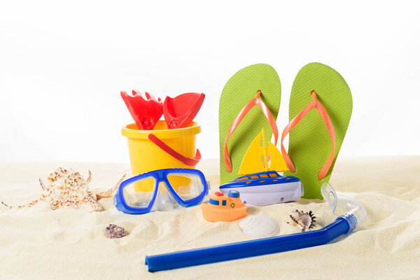 Beach toys and flip flops with diving mask in sand isolated on white