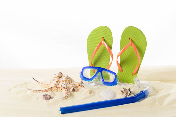 Flip flops and diving mask with seashells in sand isolated on white