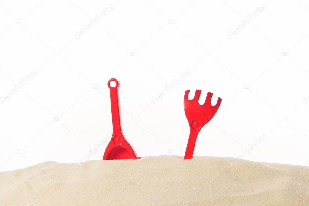 Red shovel and rakes in sand isolated on white