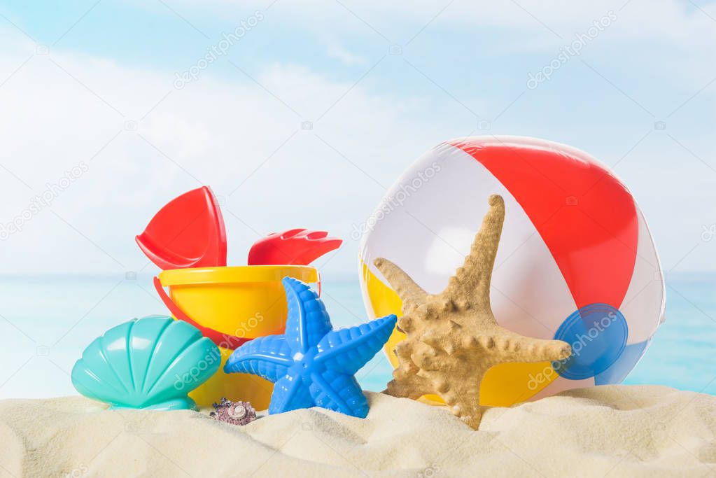 Beach ball and toys in sand on blue sky background