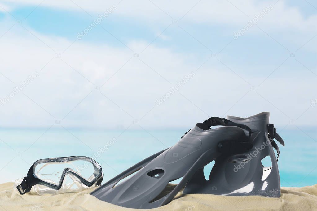 Mask and flippers in sand on blue sky background