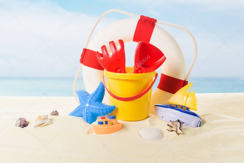 Life ring and beach toys in sand on blue sky background