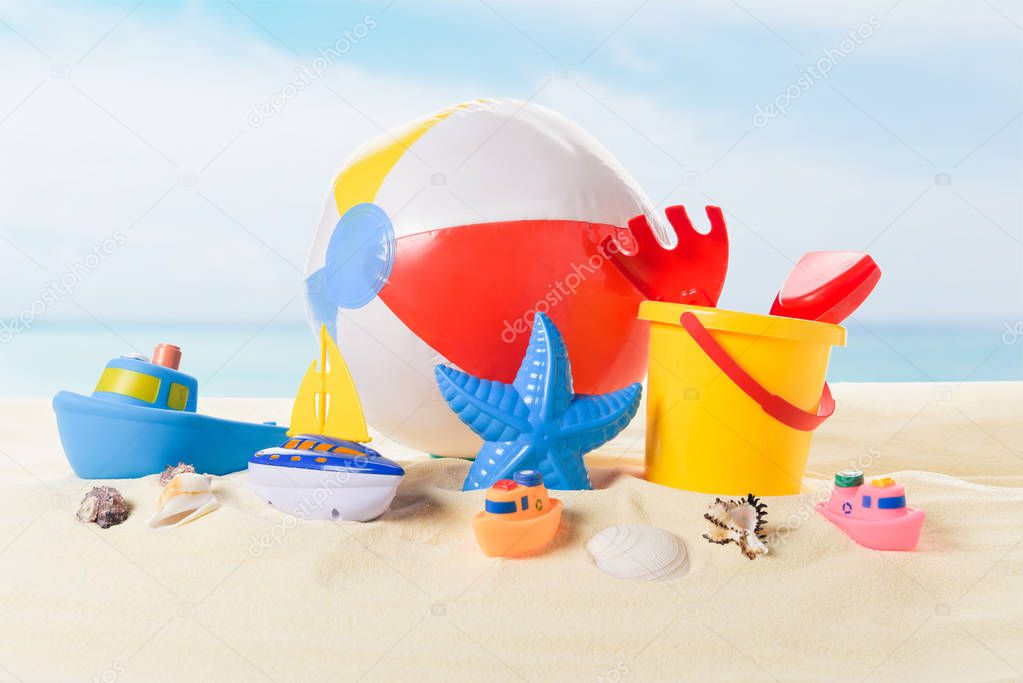 Beach ball and bucket with toys in sand on blue sky background