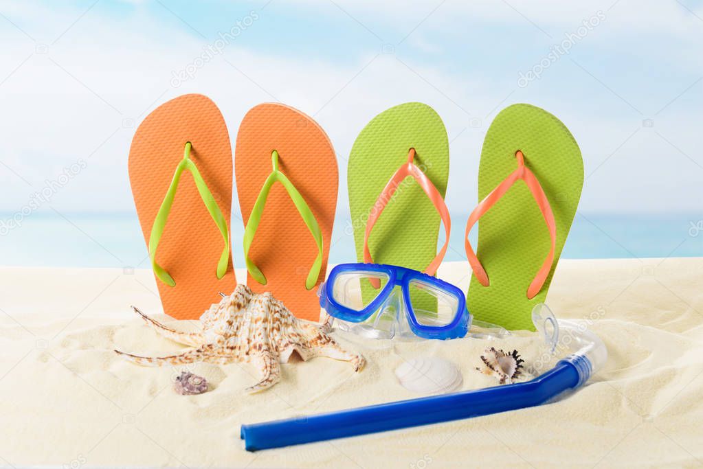 Flip flops and diving mask in sand on blue sky background