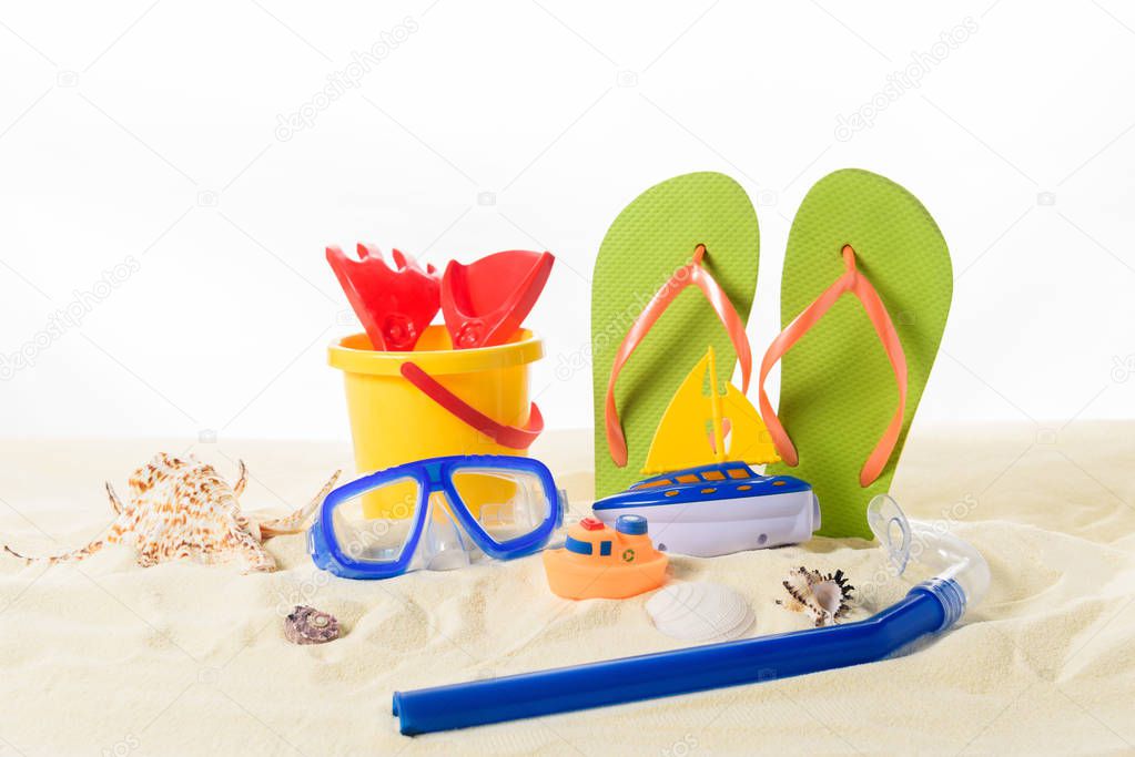 Beach toys and flip flops with diving mask in sand isolated on white