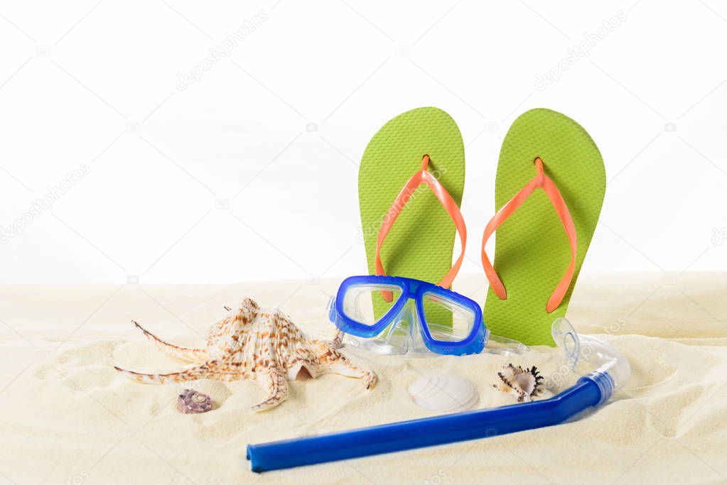 Flip flops and diving mask with seashells in sand isolated on white
