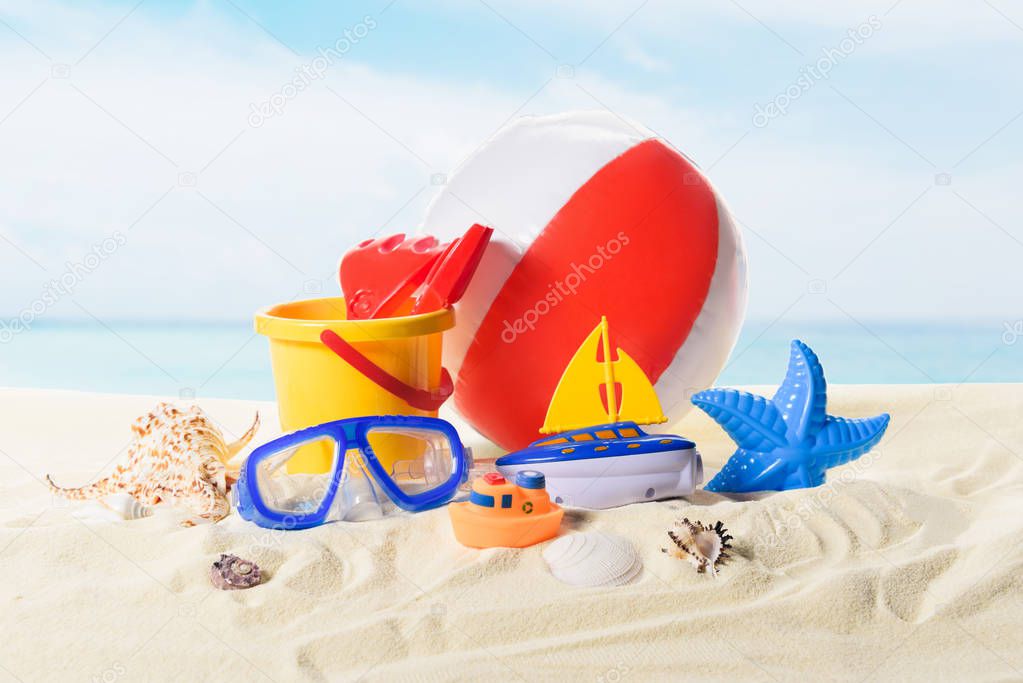 Beach ball and toys in sand on blue sky background