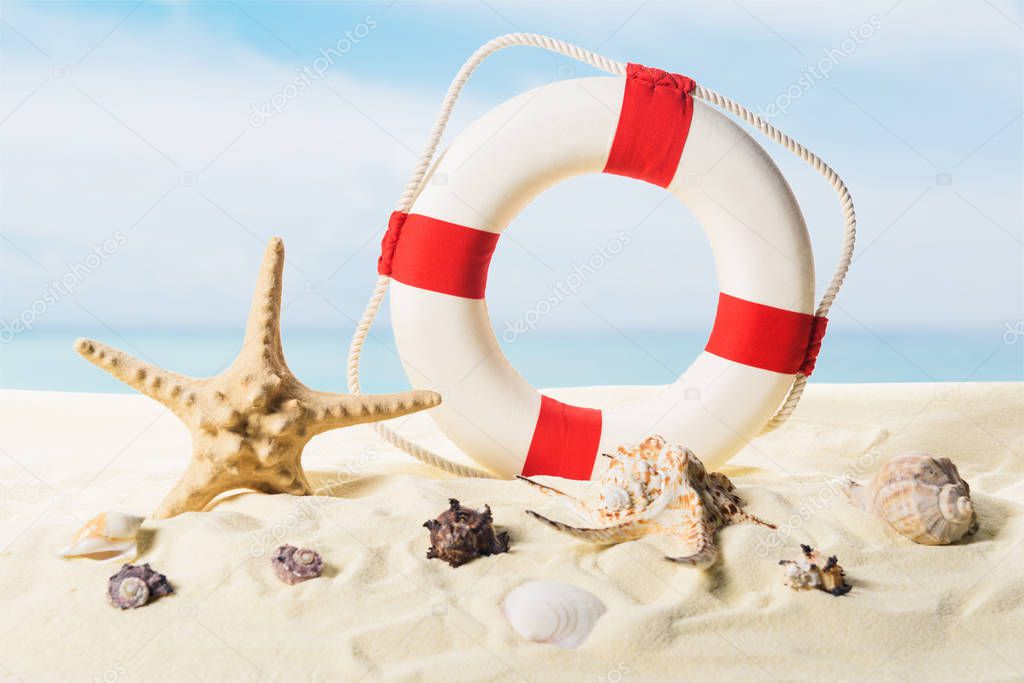 Life ring and seashells in sand on blue sky background