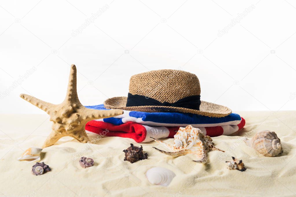Seashells and straw hat in sand isolated on white