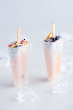 close-up view of sweet homemade popsicles with fruits and berries and ice cubes on grey   clipart