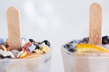 close-up view of sweet homemade ice cream with sticks in containers on grey    clipart