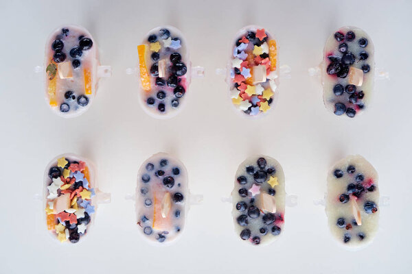 top view of tasty homemade popsicles with organic fruits and berries on grey 