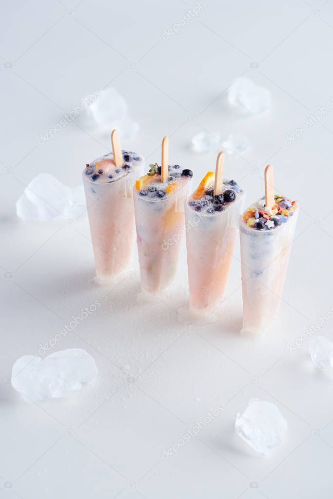 high angle view of sweet homemade popsicles with fruits and berries and ice cubes on grey   