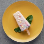 Top view of delicious fruity popsicle with green mint leaves on yellow plate on grey