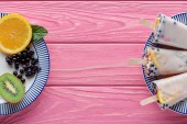 Draufsicht auf hausgemachte Eis am Stiel und frisches Obst auf Tellern auf rosa Holztisch