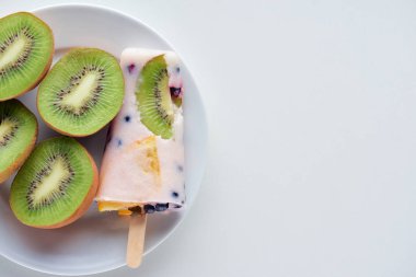 top view of delicious homemade popsicle with berries and slices of kiwi on plate on grey  clipart