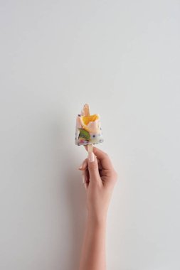 cropped shot of person holding fresh cold fruity popsicle on stick on grey  clipart