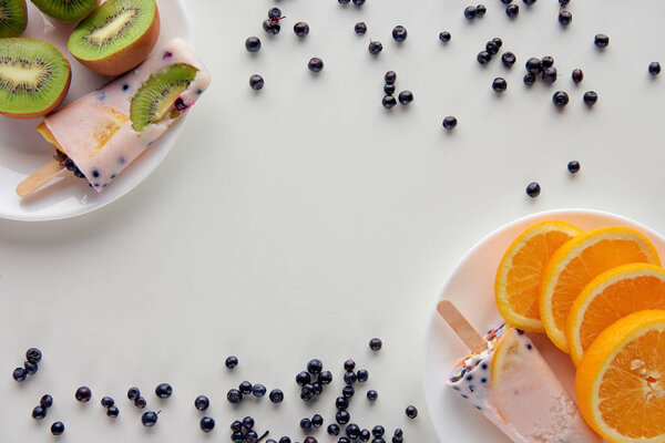 вид сверху на вкусные домашние фруктовые мороженое с ломтиками апельсина и киви на тарелках и ягоды на сером фоне
 
